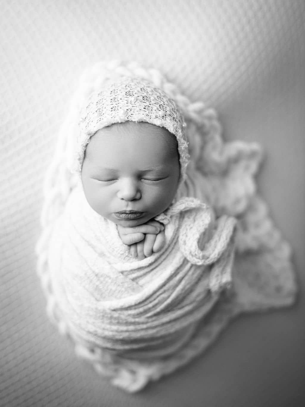 black and white photo of swaddled newborn girl in a bonnet